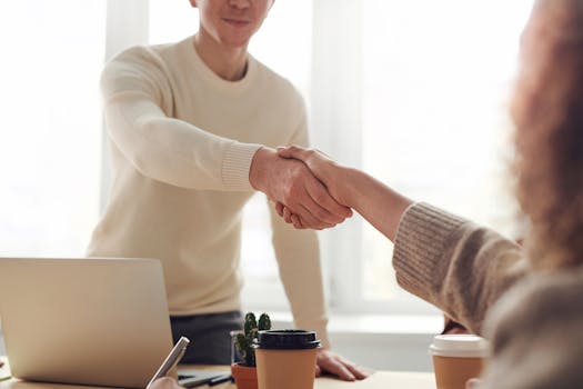 Close-up of professionals shaking hands over coffee in a modern office.